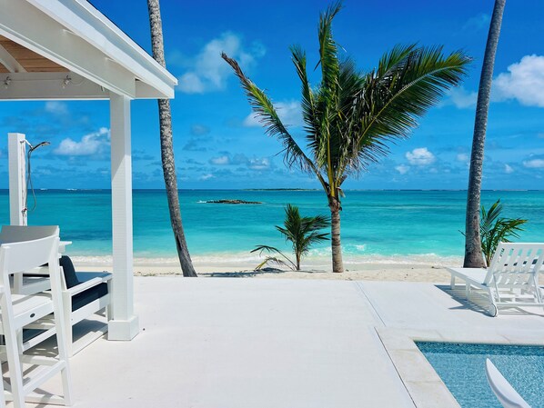 Un espace piscine situé au bord de la plage, avec des chaises longues et une vue sur l’océan.