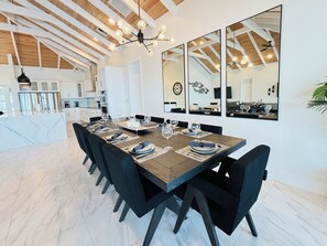 Un espace repas avec une longue table dressée pour six personnes, des chaises noires et un lustre.