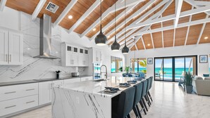 A modern kitchen with a marble island, pendant lighting, and a view of the ocean.