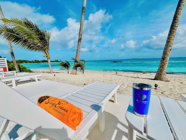 Vista mar aigua amb gandules, un got blau i una tovallola amb la inscripció 'Stay Exuma Luxury Rentals'.