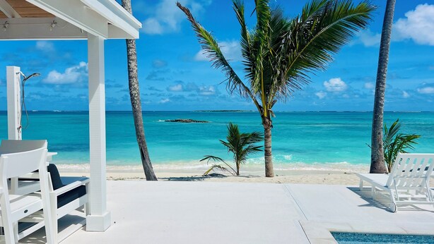A beachside pool area with white lounge chairs and a view of the ocean.