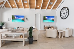 A modern living room with a sofa, coffee table, and a large clock on the wall. - Island Time - Brand New 4 bedroom Luxury House right on the Beach! (Steventon)