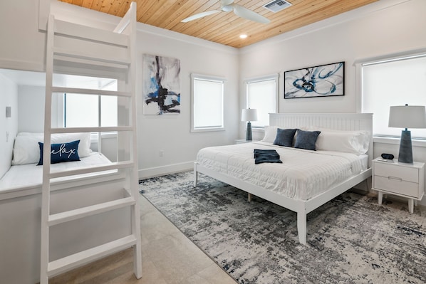 A bedroom with a bed, a nightstand, a lamp, a ladder, and artwork on the walls. - Island Time - Brand New 4 bedroom Luxury House right on the Beach! (Steventon)