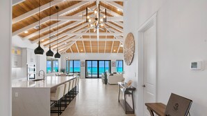 A spacious kitchen with a large island, a dining area with chairs, and a view of the ocean through large windows.