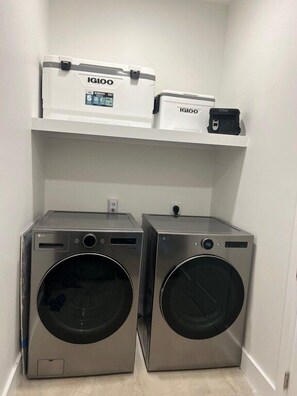 Dos lavadoras de acero inoxidable de carga frontal en un cuarto de lavado con estantes blancos arriba.