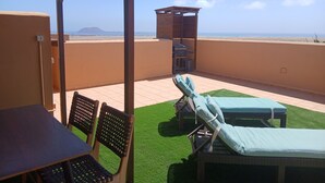 Terraza en la azotea con una mesa, sillas, una parrilla y sillones.