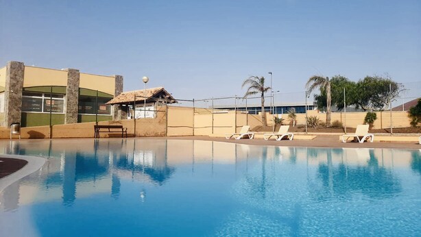 Una piscina con sillones de descanso y un edificio con techo de tejas al fondo.