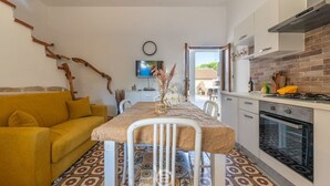 A compact kitchen with a dining area, featuring a patterned floor, a yellow sofa, and a TV mounted on the wall. - La Casa sul Mare (Su Pallosu)