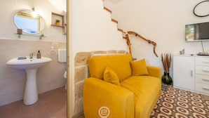 A modern bathroom with a white pedestal sink, a round mirror, a yellow sofa, and a patterned floor. - La Casa sul Mare (Su Pallosu)