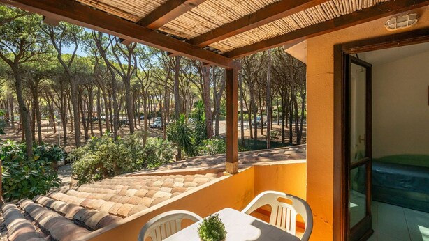 Un espacio de estar techado al aire libre con una mesa y sillas, con vistas a un paisaje boscoso.