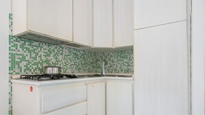 Una cocina con gabinetes blancos, una estufa a gas y azulejos verdes y blancos en el respuesto.