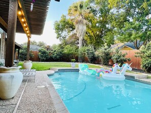 A backyard with a swimming pool, inflatable unicorn floats, and a pergola with string lights. - Heated pool & hot tub close to six flags!
 (San Antonio)