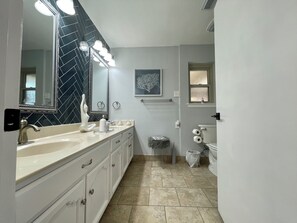 A bathroom with a large mirror, two sinks, a toilet, and a trash can. - Heated pool & hot tub close to six flags!
 (San Antonio)