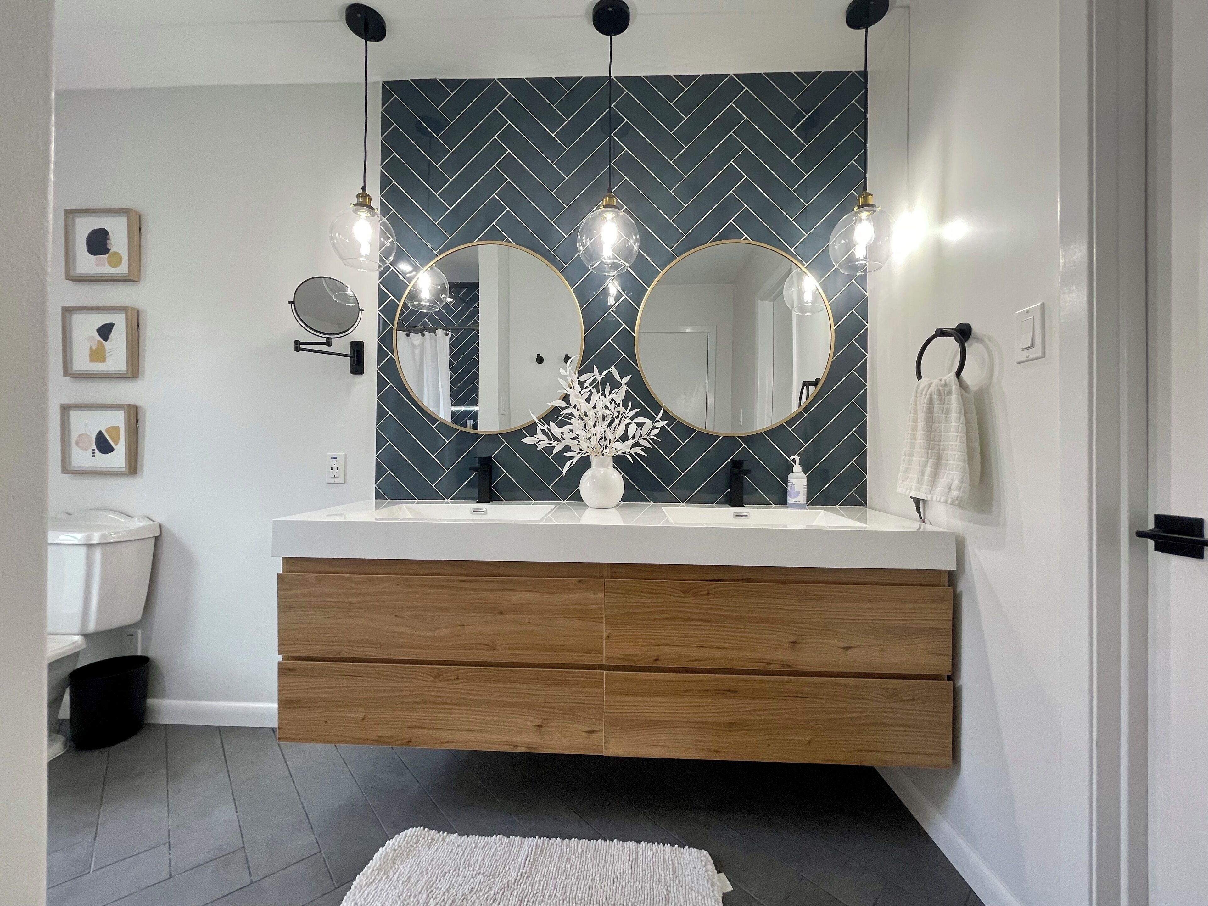 Une salle de bain moderne avec un revêtement mural en motif chevrons, un meuble-lavabo double agrémenté de miroirs ronds, un éclairage suspendu et un lavabo blanc.