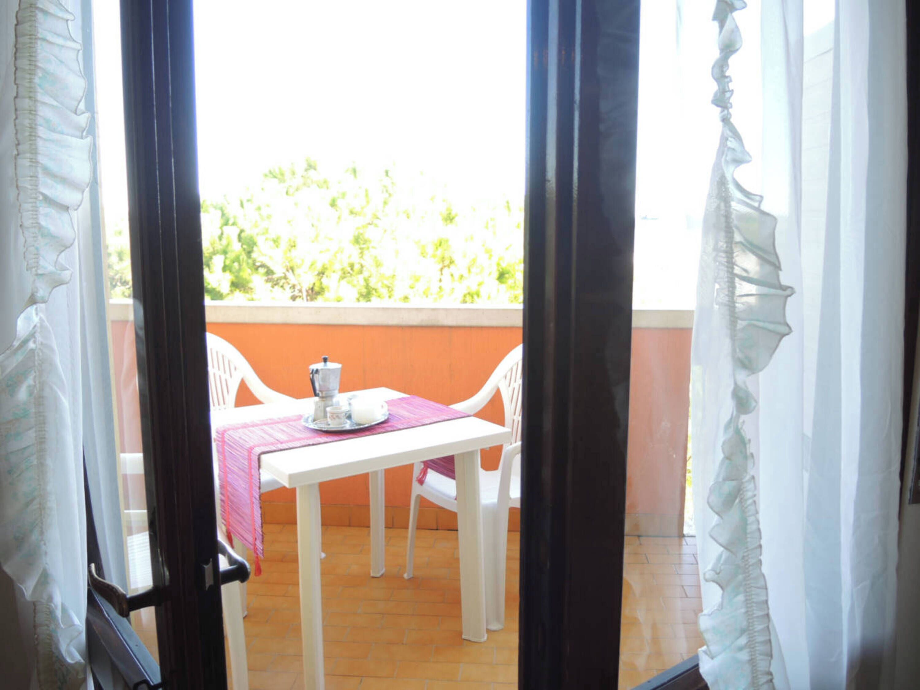 An outdoor balcony with a white table and chairs, a pink tablecloth, and a coffee pot.