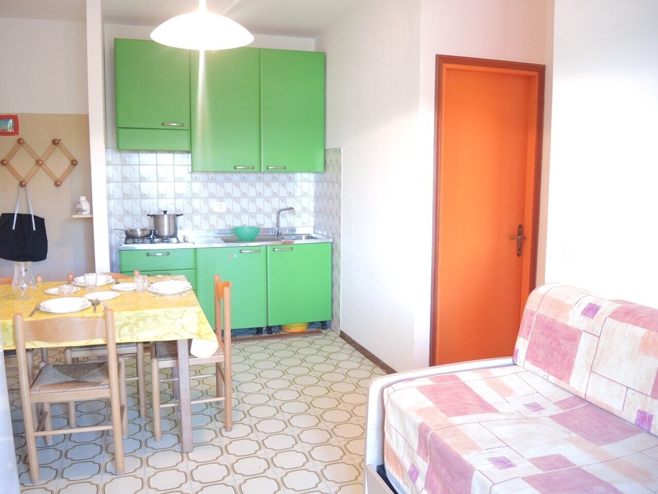 A compact kitchen with green cabinets, a dining table set with plates and cutlery, and a small sofa in the corner.
