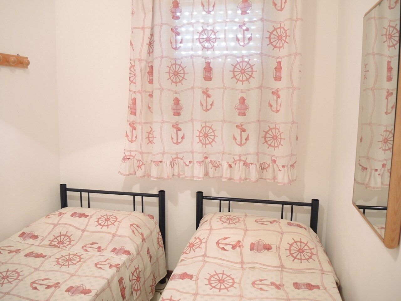 Een slaapkamer met twee eenpersoonsbedden, een raam met gordijn en een spiegel aan de muur.