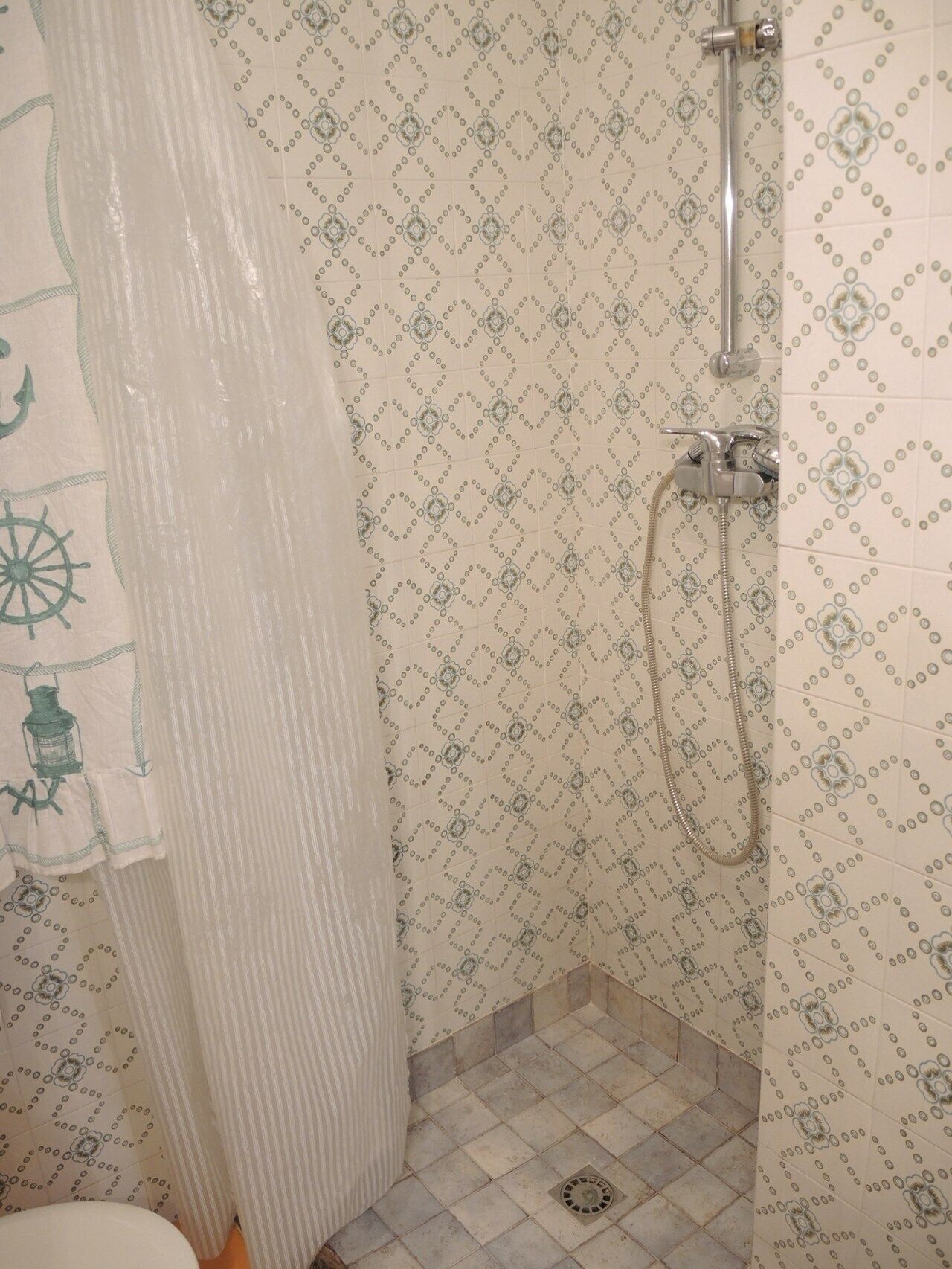A bathroom with patterned tiles, a shower, and a curtain with nautical designs.