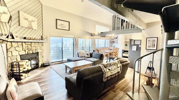 A spacious living area with a stone fireplace, a staircase, and a large window. - NEW to VRBO- LONG TERM Mountain Retreat - 2BR + LOFT Sleeps 6-8 (Silverthorne)