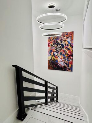 Eine Treppe mit schwarzer Handlauf und einer modernen Leuchte darüber.
