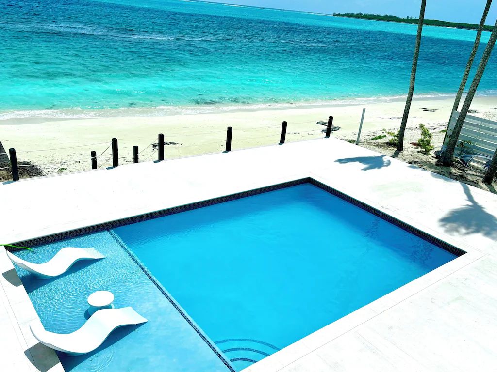 A rectangular swimming pool with a view of the ocean and beach.