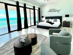 Une chambre moderne avec un grand lit, une vue sur la mer et une œuvre d’art fixée au plafond.