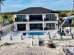 Una casa moderna de dos pisos con piscina, mobiliario exterior y vistas a la playa.