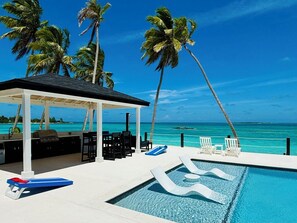 Un espace piscine avec des chaises longues, un barbecue et une vue sur l’océan.