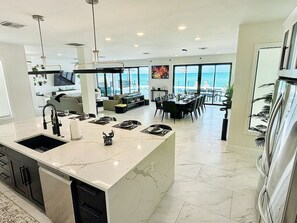 Une cuisine moderne dotée d’un grand îlot central, d’un coin repas avec des chaises et offrant une vue sur l’océan.