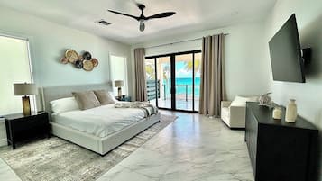 A modern bedroom with a large bed, a ceiling fan, and a view of the ocean through the sliding doors.