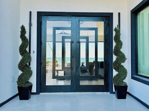 Una entrada moderna con puerta de vidrio, plantas en macetas y vista a la playa.