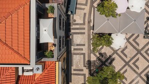 An aerial view of a building with a red-tiled roof, a paved courtyard with geometric patterns, and outdoor seating with umbrellas.
