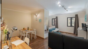 A modern living room with a sofa, a dining area with a table and chairs, and a kitchen area with a stove and counter.