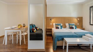 A modern hotel room with a wooden headboard, a dining area with a table and chairs, and a bed with blue bedding.