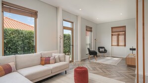Uma sala de estar ampla, com um sofá grande, um banquinho vermelho e um piso com padrão herringbone.