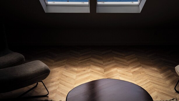 Quarto com piso de madeira em padrão herringbone, duas cadeiras pretas e um banquinho preto.