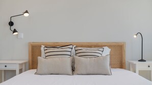 Cama bem arrumada com almofadas listradas, cabeceira de madeira e duas mesas de cabeceira com luminárias.