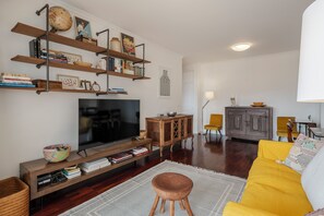 Ein Wohnzimmer mit Fernseher, Holzregalen, einem gelben Sofa und einem Essbereich mit Stühlen.