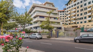 A multi-story residential building with balconies, a gated entrance, and parked cars.