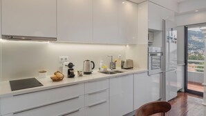 A modern kitchen with white cabinets, a stainless steel refrigerator, and a view of a cityscape through a glass door.