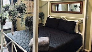Une chambre à coucher avec un lit à baldaquin, de nombreuses plantes suspendues, une fenêtre donnant sur un beau paysage et une table de chevet.