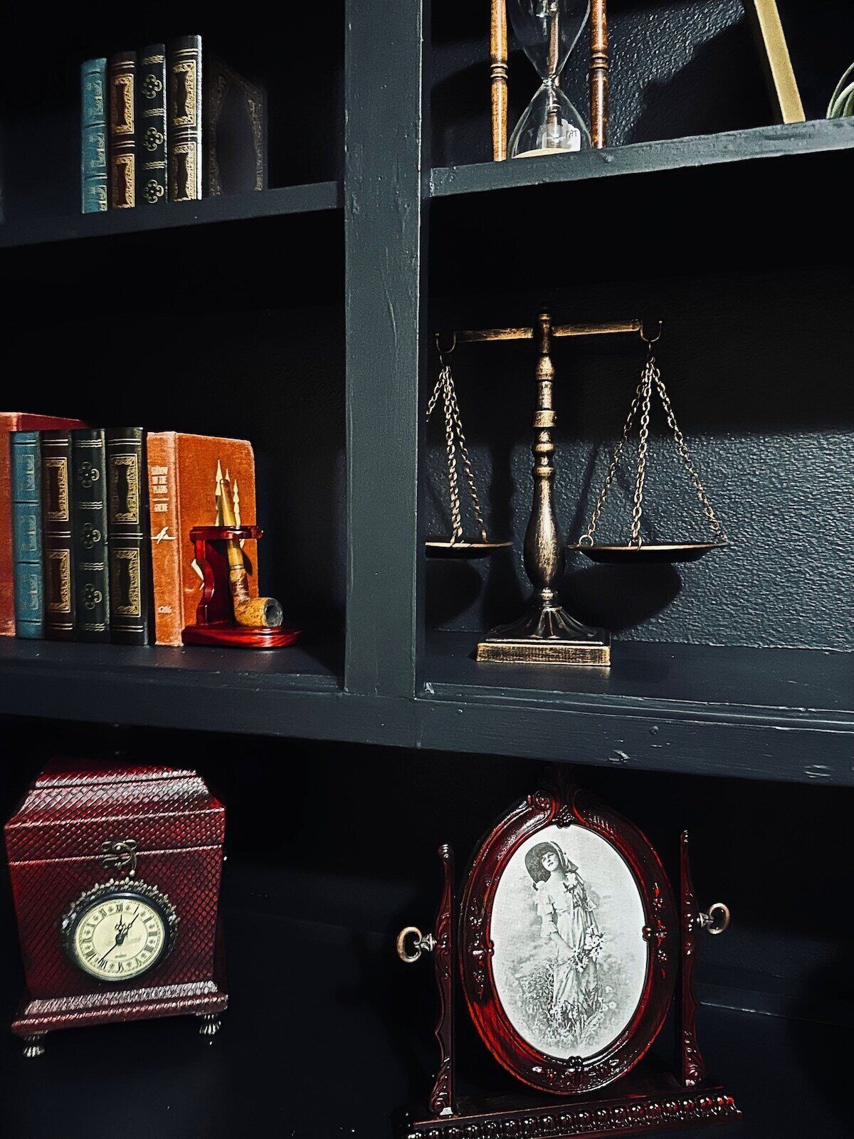 Ein Bücherregal mit Büchern, eine Waage, eine Taschenuhr und ein gerahmtes Foto.
