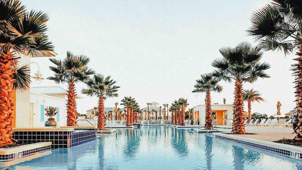 A swimming pool with palm trees and a building with a tiled pool deck. - Palm Paradise Unique Home! WALK TO BEACH! 4 POOLS! (Panama City Beach)