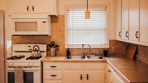 Una cocina con armarios blancos, microondas, estufa, lavabo y una ventana con persianas.