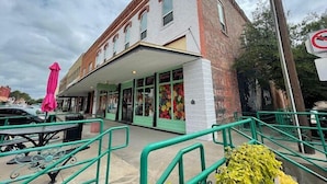 A building with a covered entrance, a brick facade, and a green railing. - Historic Downtown Loft (Waxahachie)