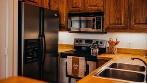 A kitchen with wooden cabinets, a stainless steel refrigerator, a microwave, an oven, and a sink. - Historic Downtown Loft (Waxahachie)