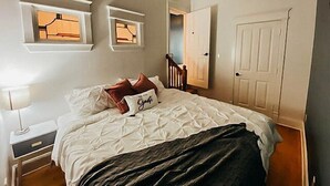 A bedroom with a bed, a nightstand, a dresser, and a door. - Historic Downtown Loft (Waxahachie)