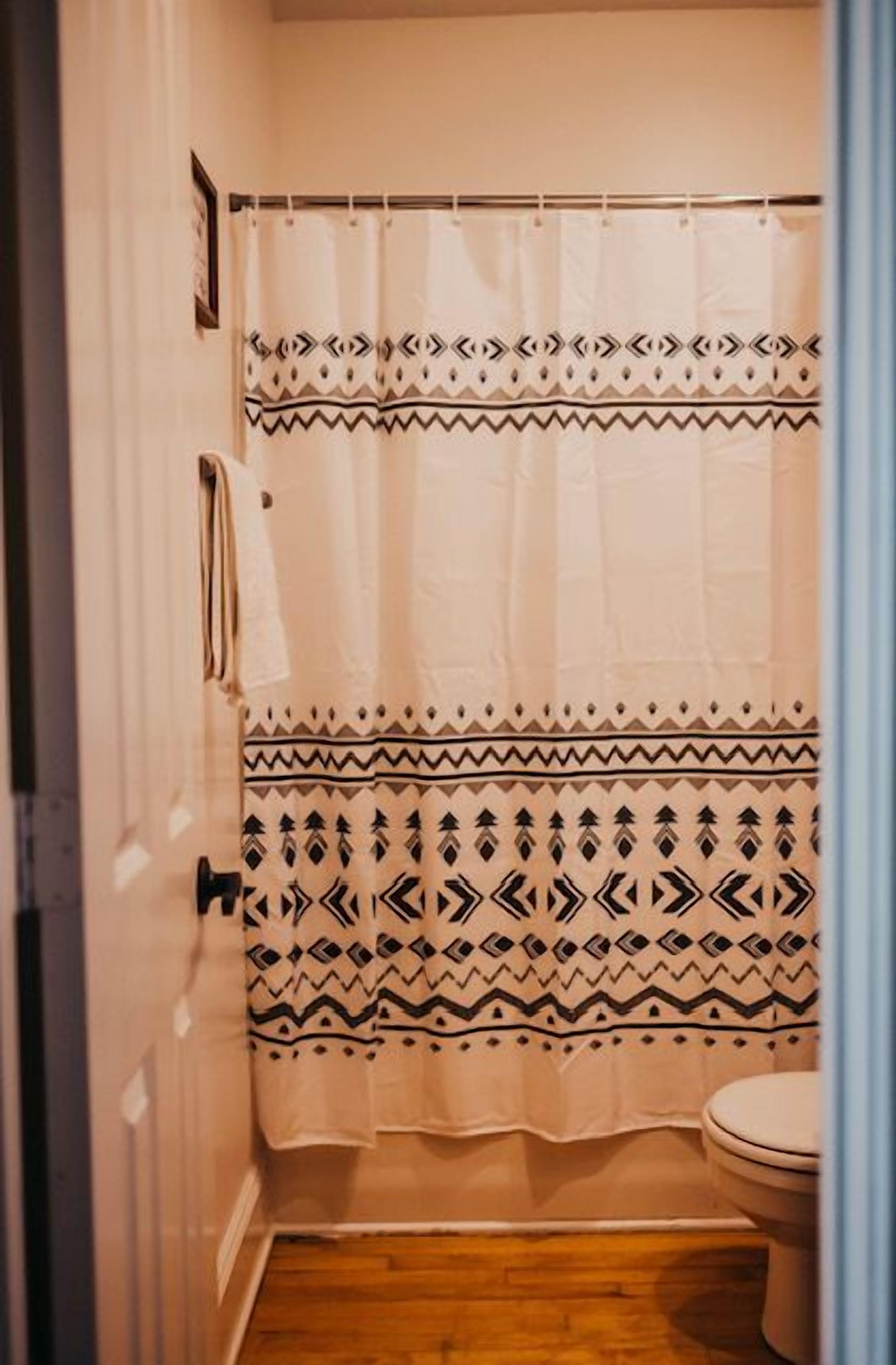 A bathroom with a shower curtain featuring a geometric pattern, a toilet, and wooden flooring.