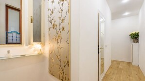 Un couloir doté d’un plancher en bois, d’un miroir fixé au mur, d’un panneau décoratif orné d’un motif d’arbre et d’une plante en pot.