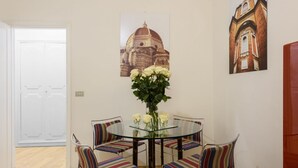 Un coin repas avec une table en verre, des chaises à rayures et un vase rempli de fleurs blanches.